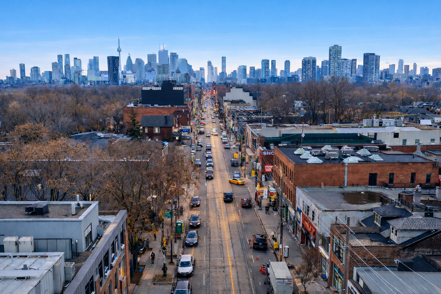 A bright elevated view of Leslieville in Toronto’s East End, showing a tree-lined street leading toward the downtown skyline under a clear blue sky